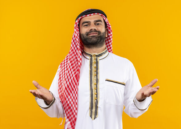 阿拉伯语身着传统服装的阿拉伯商人自信地微笑着举起双臂站在橙色的墙上传统穿着表情