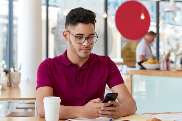 男士帅哥的照片有着满意的表情 手持现代手机 坐在舒适的自助餐厅 看视频 连接无线网络 喝外卖咖啡人与科技理念工人信息博客