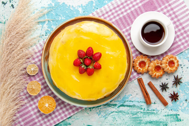 盘子俯瞰美味的蛋糕用黄色糖浆新鲜的红色草莓和一杯茶放在蓝色的表面饼干蛋糕烤甜甜的糖派茶糖浆草莓膳食