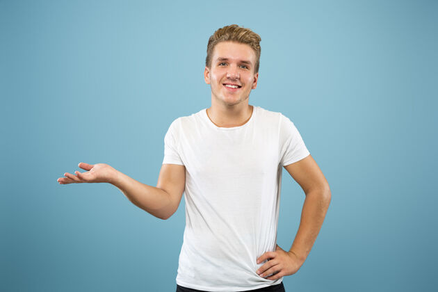 成人蓝色工作室背景上的白人年轻人半身肖像穿着衬衫的漂亮男模人类情感的概念 面部表情 销售 广告指向和展示某物人年轻肖像