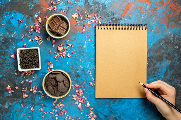 花顶视图不同的巧克力在小碗笔记本铅笔在妇女手中的蓝红色表面铅笔小顶部