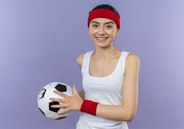 自信身穿运动服 头箍 手持足球 微笑 自信 快乐 积极向上的年轻健身女孩站在紫色的墙上运动装女孩积极