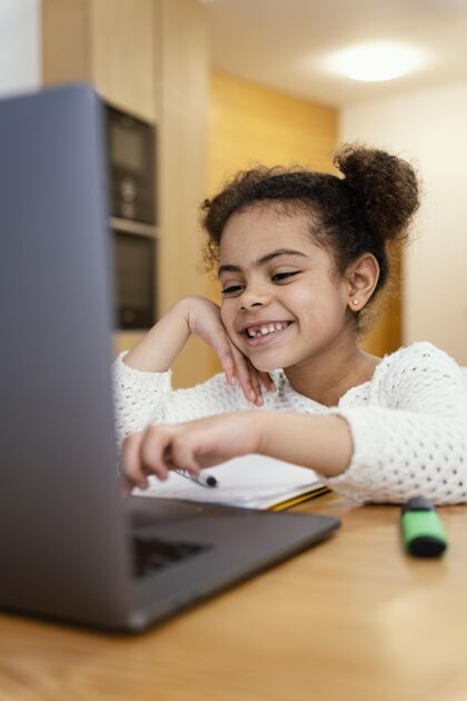 小快乐的小女孩在家里上网上学用笔记本电脑课程孩子学习