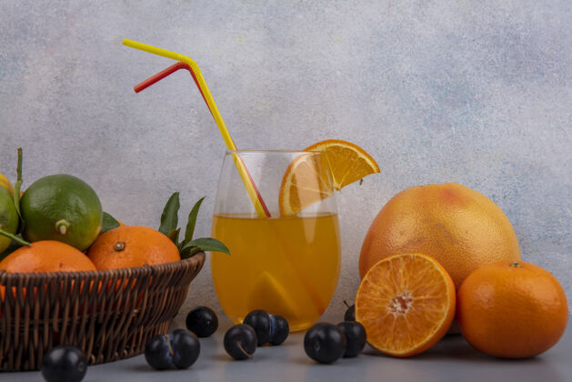 视野前视图橙色与柠檬和酸橙在一个篮子里 橙汁在一个杯子里 草莓在一个灰色的背景酸橙五颜六色玻璃