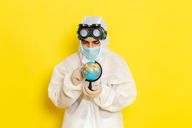 地球仪正面图：一位身着特殊套装的男科学工作者 在黄色的桌子上拿着一个小地球仪举行面具化学