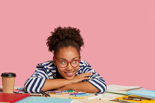 饮酒创意和灵感概念快乐微笑的非裔美国平面设计师倚在桌子旁 在笔记本上画画后喝咖啡休息 在艺术中隔着粉色的墙壁衣服蜡笔卷发