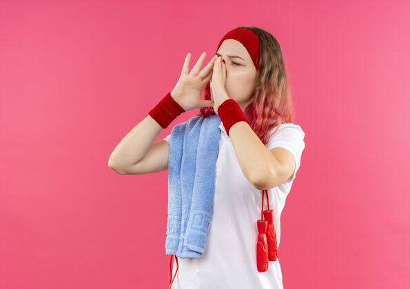 女人戴着头巾肩上戴着毛巾的运动型年轻女子 正对着站在粉红色墙上的手掌靠近嘴巴的人喊叫人年轻人电话