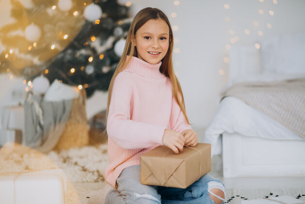举行可爱的女孩拿着圣诞礼物在圣诞树旁乐趣传统节日
