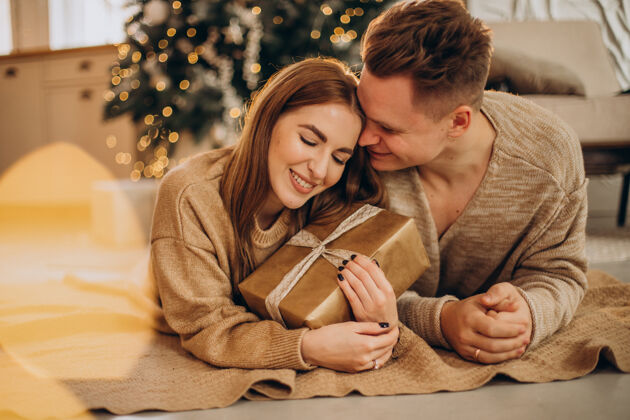 关系一对年轻夫妇在圣诞树旁互相制作礼物家庭圣诞一起