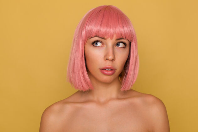 女人年轻漂亮的蓝眼睛粉红色头发的女性 短发时髦 站在芥末墙上 若有所思地向上看沉思欧式头发