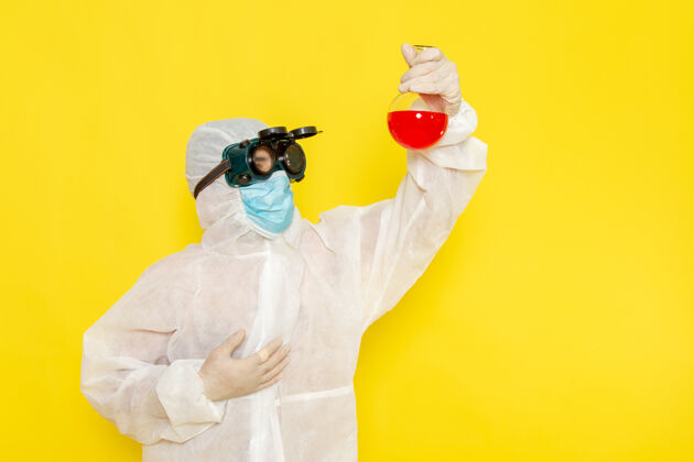 特别正面图穿着特殊防护服的男科学工作者拿着黄色表面上有红色溶液的烧瓶溶液科学服装