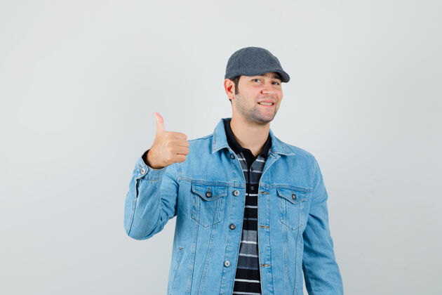 时尚年轻人穿着夹克 戴着帽子 竖起大拇指 看上去很高兴 正面照肖像休闲夹克