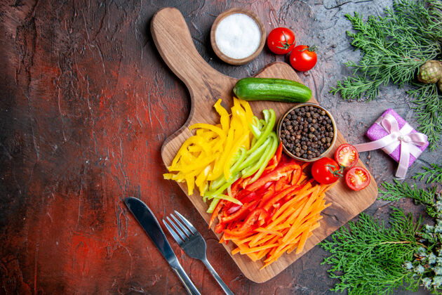 胡椒顶视图五颜六色的切辣椒黑胡椒西红柿黄瓜在砧板上盐叉子和刀小礼物在深红色的桌子上辣椒观点叉子