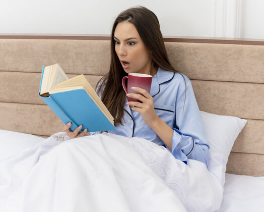 卧室穿着蓝色睡衣躺在床上的年轻漂亮女人咖啡书年轻