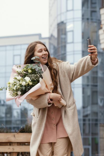 开花优雅的女人拿着花束在外面 用智能手机自拍春天户外移动