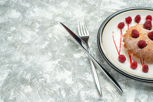 钢笔俯瞰浆果蛋糕在白色椭圆形盘子交叉叉和餐刀在灰色表面自由空间椭圆盘子