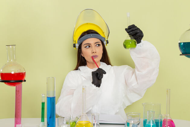 溶液正面图：穿着特殊防护服的女化学家坐在桌子前面 在绿色的表面上与她们一起工作套装女实验室