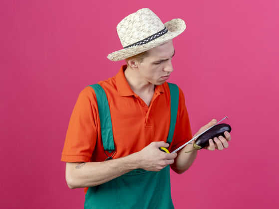 帽子年轻的园丁穿着连体衣戴着帽子拿着茄子量着呢脸测量男人