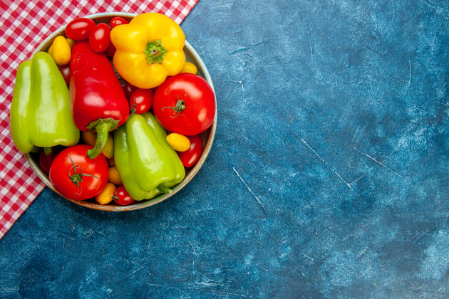 铃铛顶视图新鲜蔬菜樱桃西红柿不同颜色甜椒西红柿cumcuat在碗里红色和白色格子桌布在蓝色的桌子上复制的地方地方胡椒樱桃