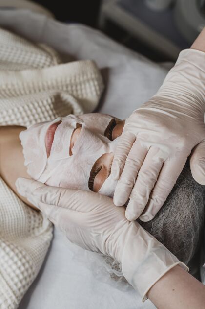 护理在健康中心接受皮肤面膜治疗的年轻女子化妆品面部垂直