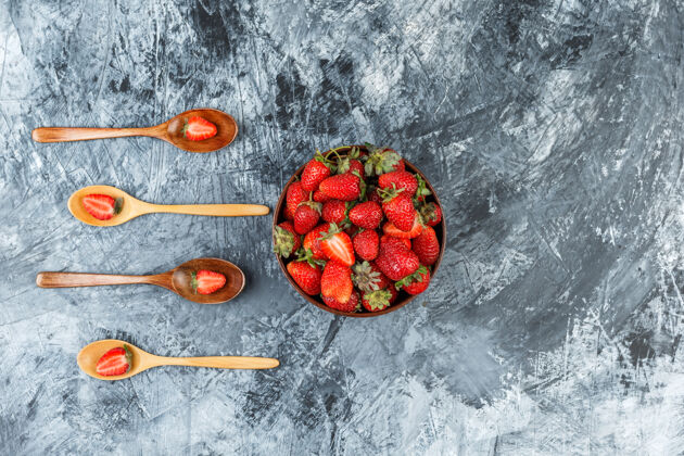 美味俯视图一碗草莓和四个木勺在深蓝色大理石表面水平木头草莓早餐