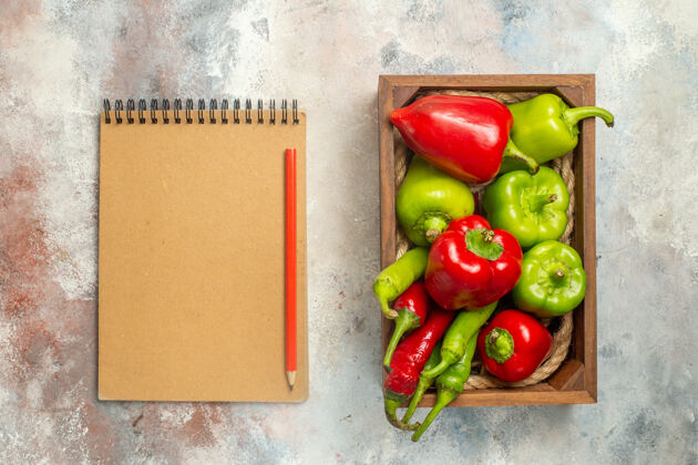甜椒顶视图红椒和青椒木盒中的辣椒笔记本裸体表面上的红色铅笔蔬菜胡椒顶部