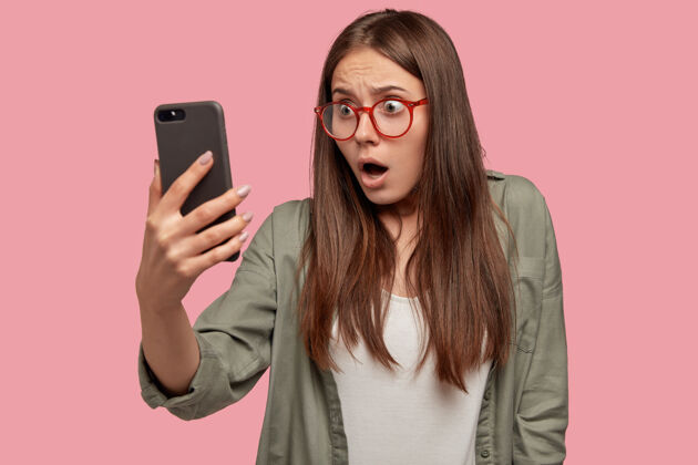 衬衫震惊的女人在智能手机屏幕上看到尴尬的画面衣服凝视小工具