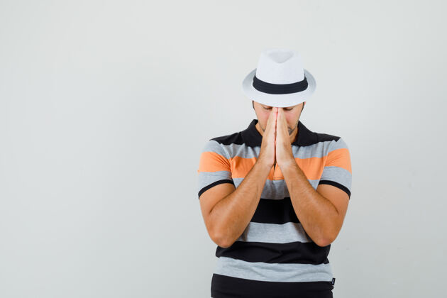 脸一个年轻人穿着条纹t恤 戴着帽子 做着祈祷的手势 他看起来很专注 正前方的视野文本空间朋友商人手势