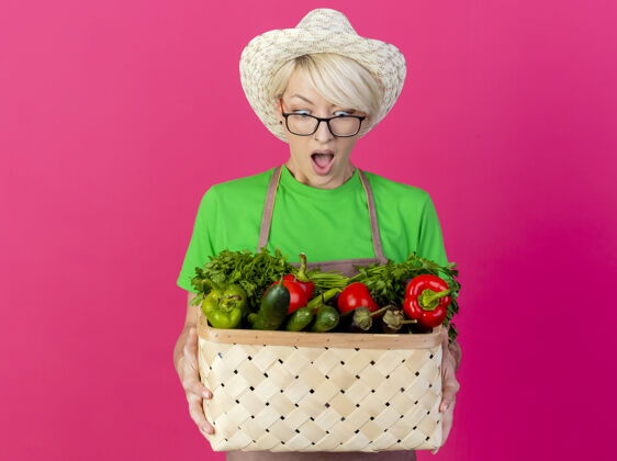 板条箱一位年轻的园丁 围着围裙 戴着帽子 手里拿着装满蔬菜的箱子围裙花园头发