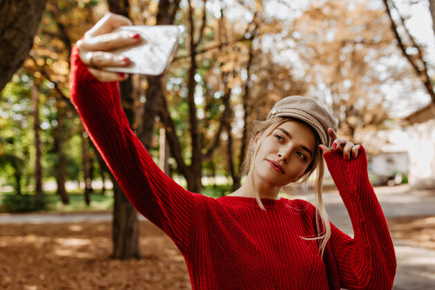 小美丽的金发女郎在秋季公园自拍穿着红毛衣戴白帽子的迷人女士拍照帽子金发玩耍
