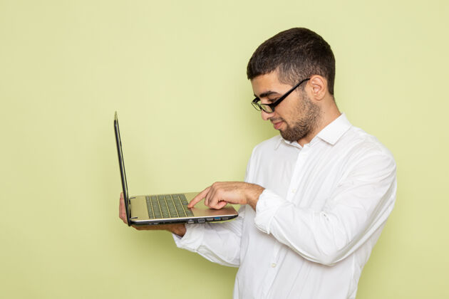 商务身穿白衬衫的男办公室工作人员正拿着笔记本电脑站在浅绿色的墙上工人衬衫办公室