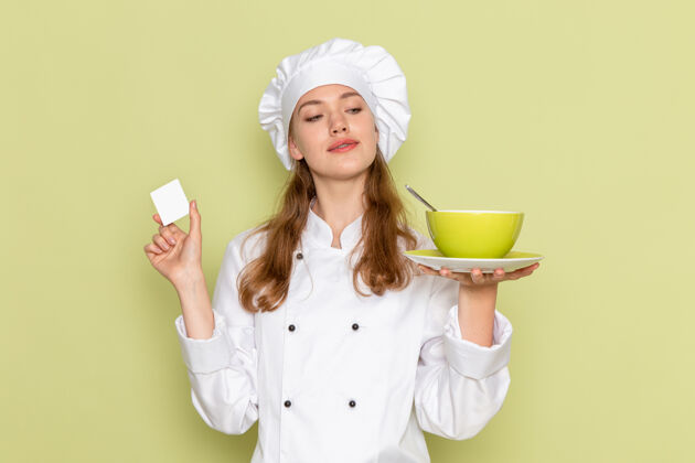 烹饪身着白色厨师服的女厨师正拿着绿色盘子站在绿色墙上成人厨房举行