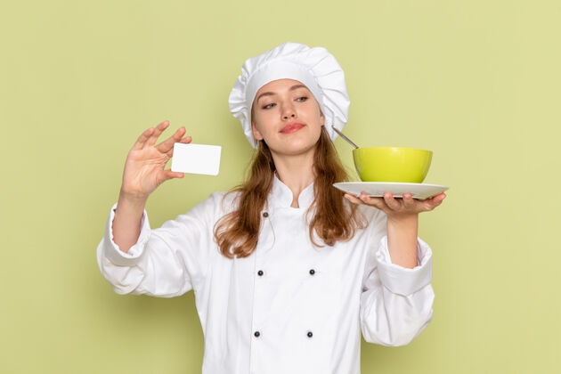 淋浴帽身穿白色厨师服的女厨师正对着绿色的墙壁 手里拿着绿色的盘子和卡片女快乐西装