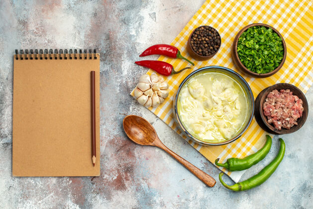 碗俯瞰杜什巴拉饺子汤碗大蒜辣椒木勺碗肉辣椒和绿色笔记本在裸体桌上午餐盘子肉
