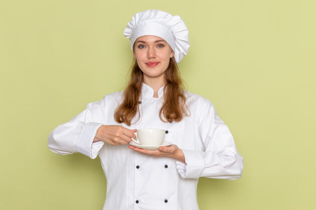 人身着白色厨师服的女厨师手持绿色墙壁上的杯子的正视图护士前面厨房