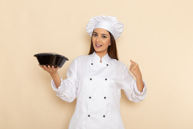 成人身穿白色厨师服的年轻女厨师正拿着碗站在白墙上医生厨房专业