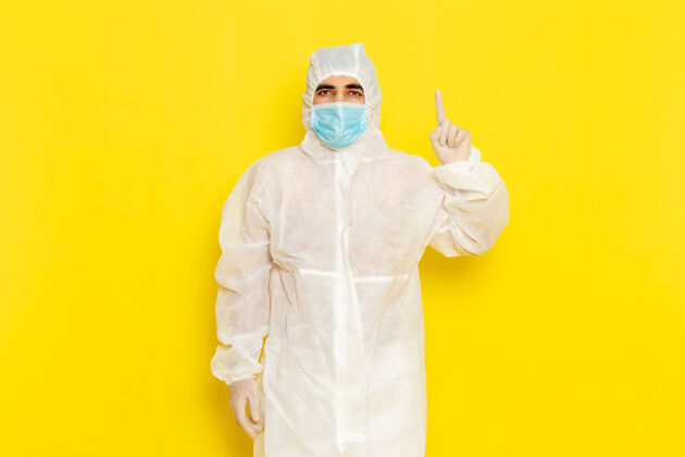 危险身穿白色特殊防护服 戴着口罩的男性科学工作者的正面图摆在黄色的墙上正面伪装掩护