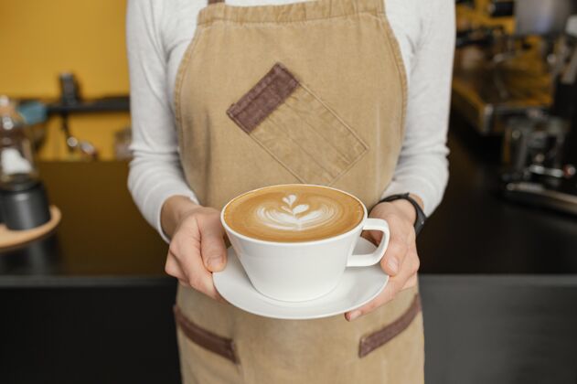 就业女咖啡师手持装饰过的咖啡杯的正面图服务员职业工作