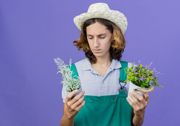 穿着年轻的园丁 穿着连体衣 戴着帽子 手里拿着盆栽植物困惑花园连身衣