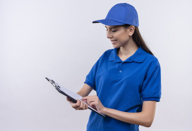 剪贴板穿着蓝色制服 戴着帽子的年轻送货员面带微笑地看着剪贴板上的空白页制服年轻女孩