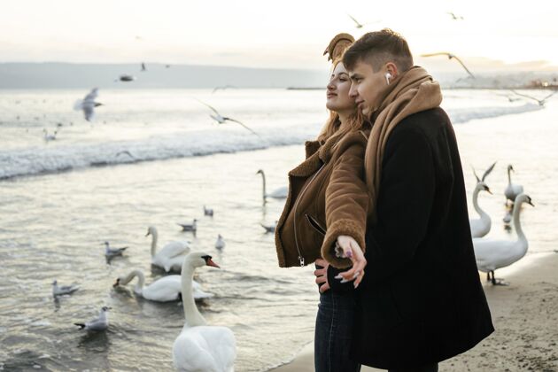 鸟冬天在沙滩上用耳机听音乐的情侣冬天户外季节