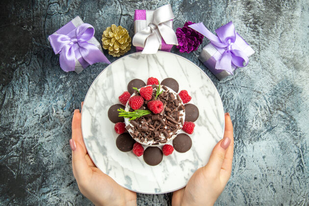 覆盆子俯瞰巧克力芝士蛋糕与覆盆子在椭圆形盘子在妇女手中圣诞礼物灰色表面免费空间巧克力芝士蛋糕盘子椭圆形