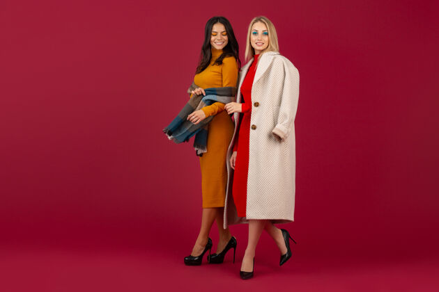 时尚两位穿着秋冬时装礼服和外套的时尚女性在红墙上孤零零地摆着姿势衣服魅力夹克