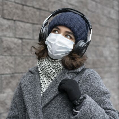 妇女戴着医用口罩的女人在城里听音乐耳机防护新常态