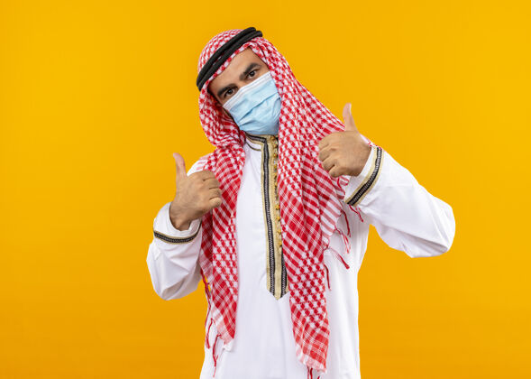 站立身着传统服装和面罩的阿拉伯商人自信地站在橙色的墙上竖起大拇指传统表情商务人士
