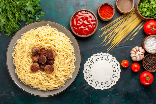 烹饪顶视图煮熟的意大利面食与肉丸和不同的调味品在深蓝色的表面膳食盘子早餐
