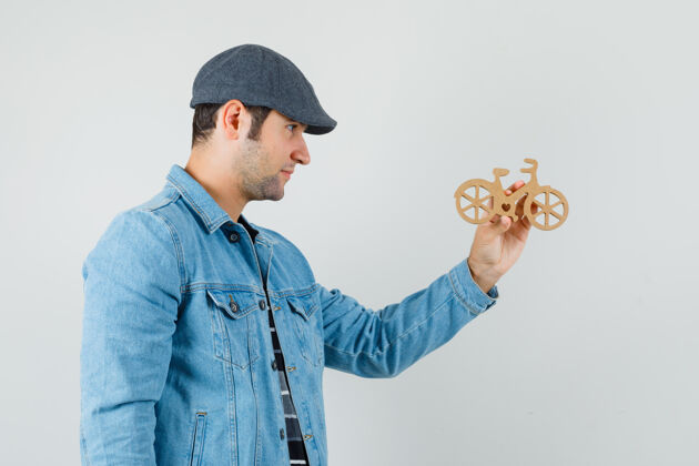 木头年轻人看着戴着帽子 t恤衫 夹克衫的木制玩具自行车 神情专注商人男性胡须