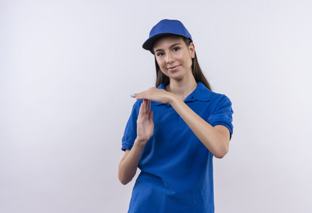 年轻穿着蓝色制服 戴着帽子的年轻送货女孩看着相机 用手做着暂停的手势手时间使