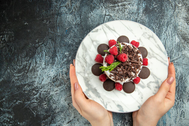 盘子俯瞰芝士蛋糕与巧克力在椭圆形盘子上 在女人手上灰色表面自由的地方女士美味顶部