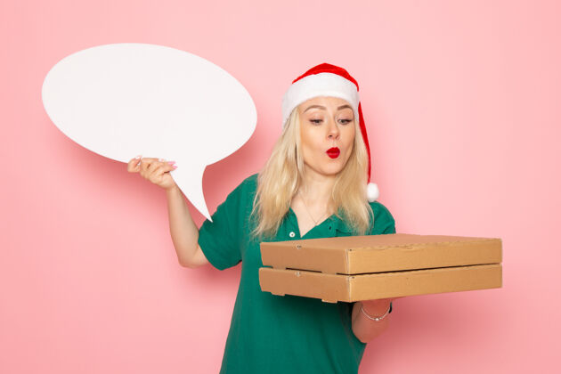 大正面图年轻女性手持白色大牌子和食品盒在粉色墙上拍照工作新年假期工作快递年轻的女性圣诞节工作